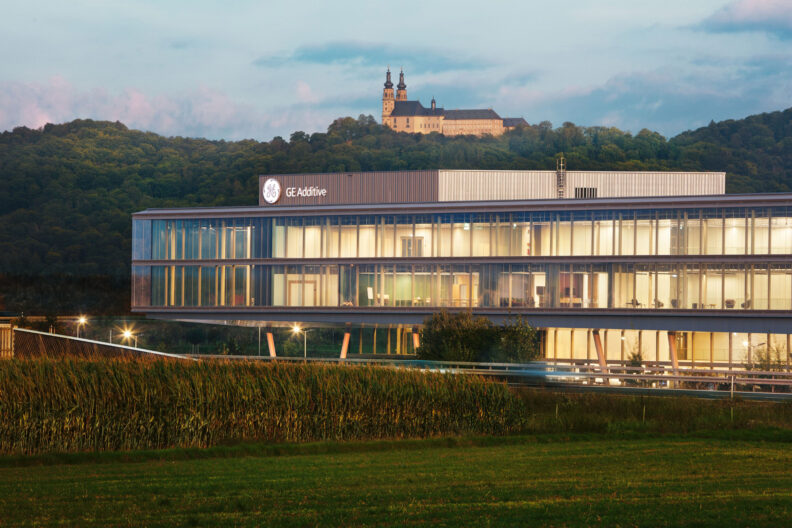 2022_B23_2021_10_01_Schrägle_2 Außenperspektive Einbindung der Umgebung mit Burg im Hintergrund in der Gesamtbild des GE Additive Lichtenfels Campus