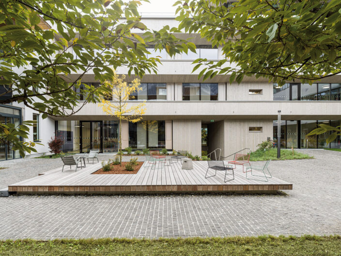 Au&szlig;enperspektive Innenhof mit Holzterrasse und Sitzm&ouml;glichkeiten Umgeben von Begr&uuml;nung der Swarovski Optik Verwaltung und Produktion